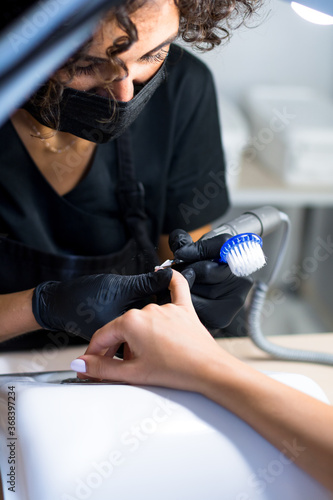 manicurist master in black gloves and mask is making manicure with a manicure drill apparatus
