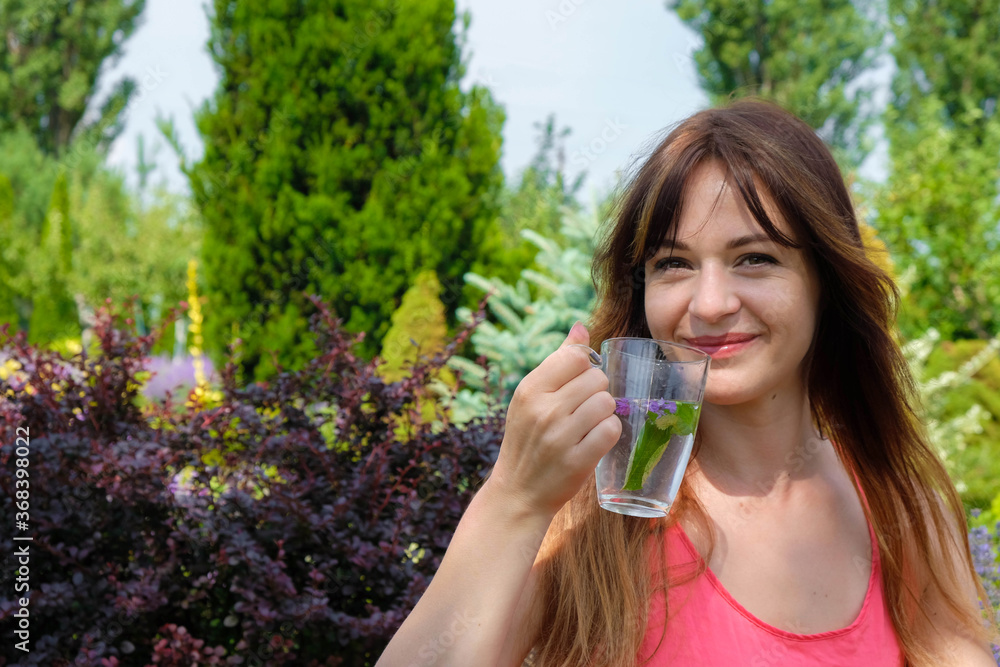 Smiling young woman with long hair with a glass of herbal tea on the background of the morning garden in Ukraine. Copy space.