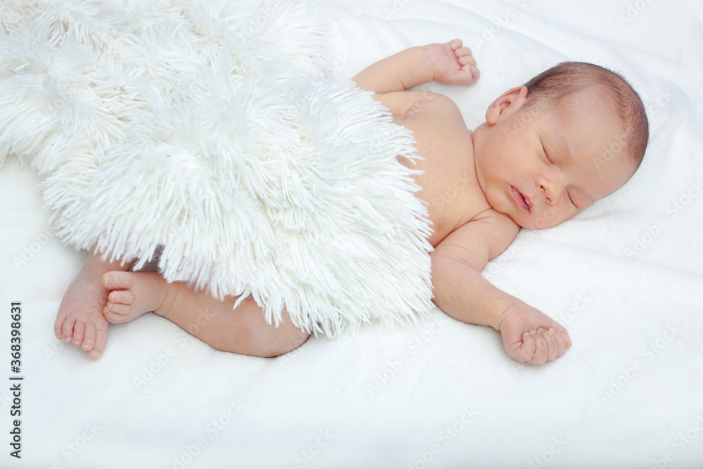 The newborn sleeps under a white fluffy blanket. The lovely newborn is sleeping peacefully. The baby is lying on his back with his hands raised up under a fluffy blanket. The newborn sleeps under a white fluffy blanket. The lovely newborn is sleeping peacefully. The baby is lying on his back with his hands raised up under a fluffy blanket.
