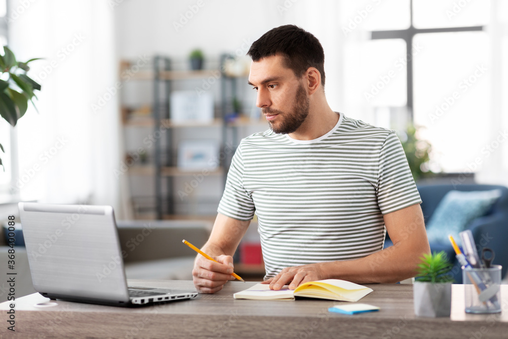 Fototapeta premium remote job, technology and people concept - young man with notebook and laptop computer working at home office