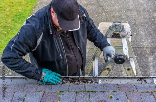 Man on top of ladder cleaning dirt from roof gutter on building - his hand in messy gloves - view from the top of the roof