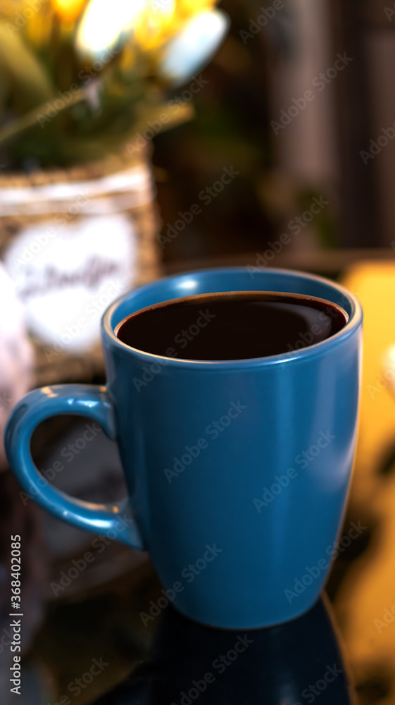 Fototapeta premium Evening coffee. Blue cup with coffee, open book and mobile phone, evening light, sunset, dusk. Atmospheric, cozy evening in the garden, green leaves, conversation. Warm light, blur bokeh.
