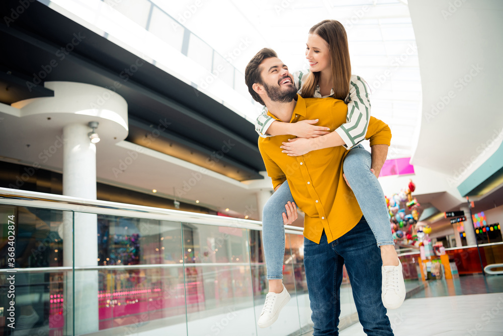 Photo of attractive lady handsome guy couple visit shopping store mall together walking piggyback carry pose having fun playing wear casual jeans shirt outfit indoors