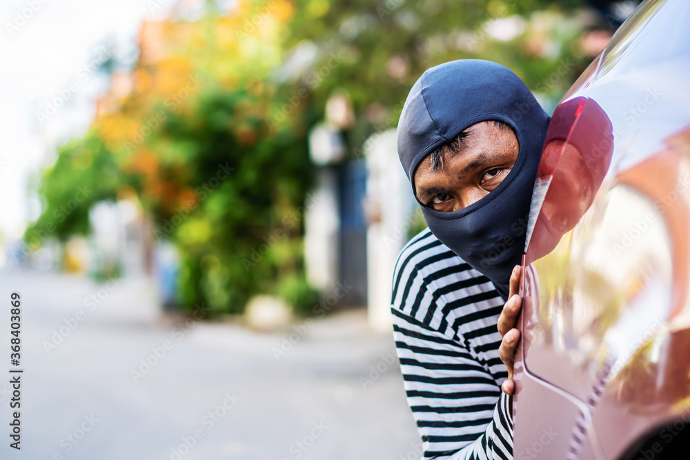 The robber wearing a black head are secretly behind the car to prepare a robbery, Planning a robbery, to crime concept.. The robber wearing a black head are secretly behind the car to prepare a robbery, Planning a robbery, to crime concept..