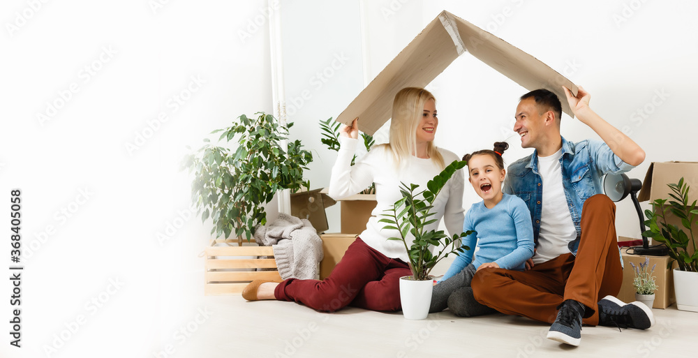 Happy family sitting on wooden floor. Father, mother and child having fun together. Moving house day, new home and design interior concept Happy family sitting on wooden floor. Father, mother and child having fun together. Moving house day, new home and design interior concept