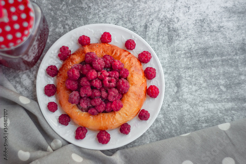 Cheesecake bun with large garden raspberries on a white plate, shot close-up