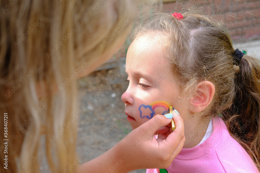 Artist painting a rainbow on girl's face. face are or face painting