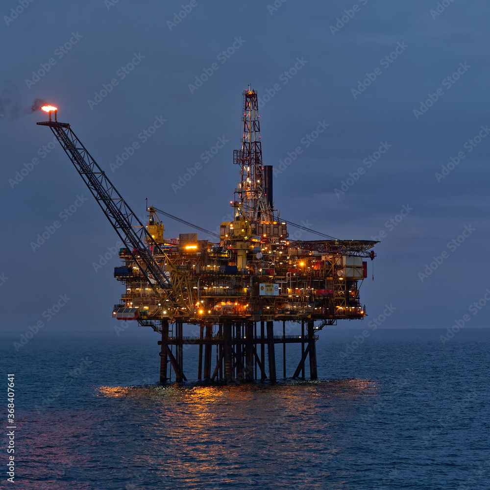 The Gannet A Oil Platform in the twilight of a Summers evening in a very calm North Seam with its lights on, and flare stack burning.