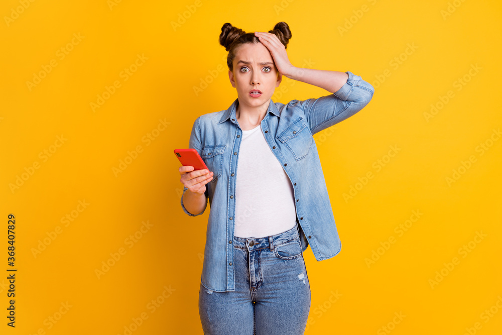 Photo of crazy teen lady two buns hold telephone speechless read comments blog open mouth notification bad news hand touch head wear casual denim shirt isolated yellow color background Photo of crazy teen lady two buns hold telephone speechless read comments blog open mouth notification bad news hand touch head wear casual denim shirt isolated yellow color background