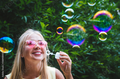 Young woman blows bubble blower in the street. Close-up portrait. Happiness and positive emotions concept