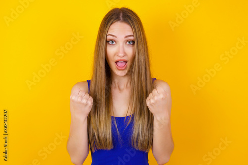 Caucasian young woman rejoicing her success and victory clenching her fists with joy.Lucky woman with hat being happy to achieve her aim and goals.Positive emotions, feelings.