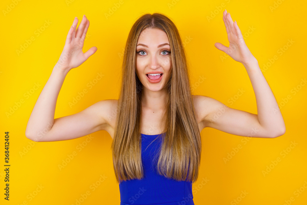 Portrait of beautiful brunette female looks with excitement at camera, keeps hands raised over head, notices something unexpected, isolated over gray wall. Lovely woman reacts on sudden news. Portrait of beautiful brunette female looks with excitement at camera, keeps hands raised over head, notices something unexpected, isolated over gray wall. Lovely woman reacts on sudden news.