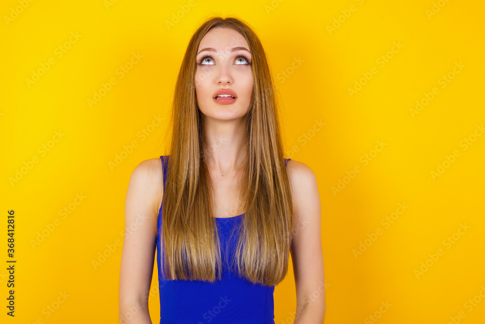 portrait of mysterious charming female with straight hair looking up with enigmatic smile. Beautiful smiling girl looking up standing against gray wall. portrait of mysterious charming female with straight hair looking up with enigmatic smile. Beautiful smiling girl looking up standing against gray wall.