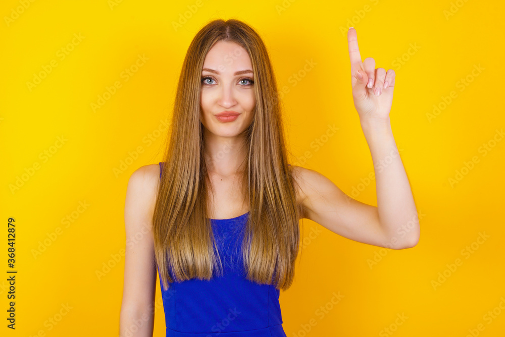 Fototapeta premium Young caucasian woman standing against gray wall showing and pointing up with fingers number one while smiling confident and happy.