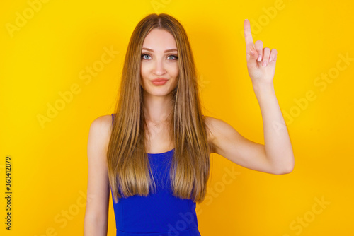 Young caucasian woman standing against gray wall showing and pointing up with fingers number one while smiling confident and happy.
