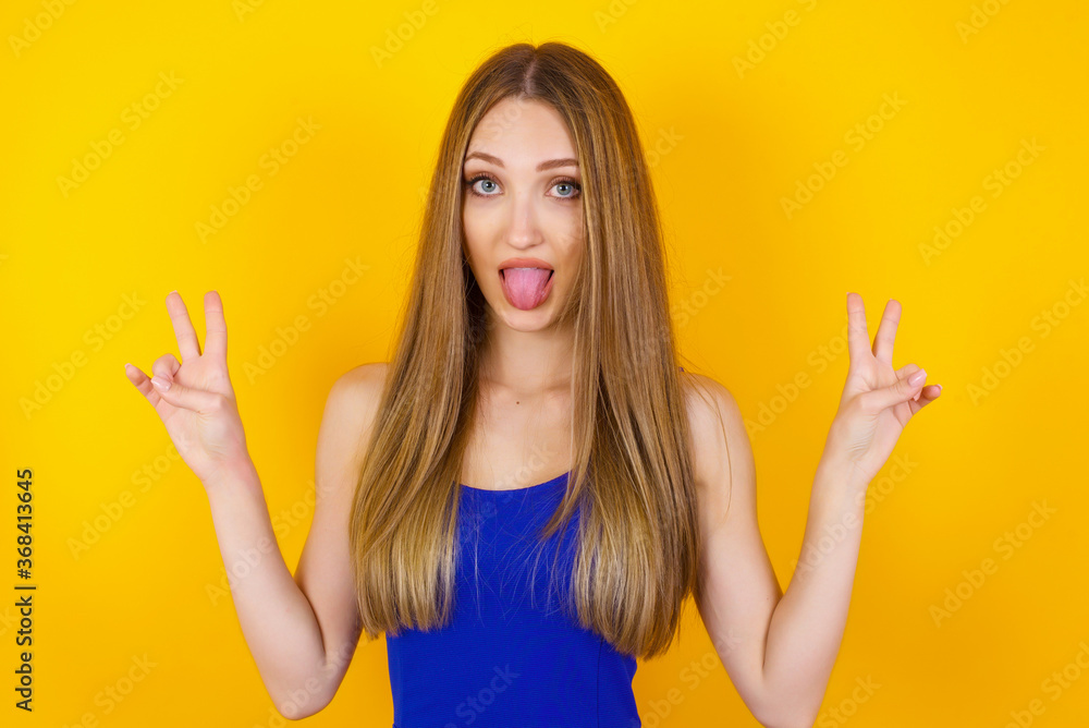 Indoor portrait of young caucasian female isolated on gray background with optimistic smile, showing peace or victory gesture with both hands, looking friendly. V sign. Indoor portrait of young caucasian female isolated on gray background with optimistic smile, showing peace or victory gesture with both hands, looking friendly. V sign.