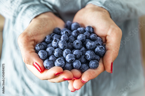 Close up of female hands holding group of fresh blueberries.