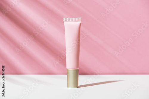 Obraz na płótnie Pink tube of soft organic natural eye cream with golden cap on white pink background, palm leaf shadow. Summer facial product, sun lotion. Women's hygiene cosmetic accessory for skincare. Copy space. w salonie