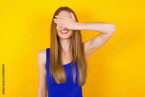 Happy Caucasian young woman closing eyes with hand going to see surprise prepared by boyfriend standing and smiling in anticipation for something wonderful. Young lady covering face with hand.