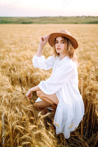 Young woman  in white linen dress and hat enjoying a sunny day in a golden wheat field. Summer, beauty, fashion, glamour, lifestyle concept. © maxbelchenko