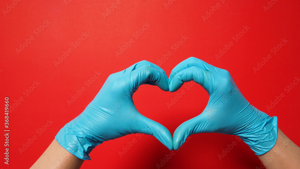 A Hand is doing heart or love hand sign and wear blue surgical gloves or latex gloves on red background. A Hand is doing heart or love hand sign and wear blue surgical gloves or latex gloves on red background.