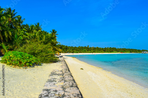 Fototapeta Naklejka Na Ścianę i Meble -  Sunny beach with white sand, coconut palm trees and turquoise sea. Summer vacation and tropical beach concept. Overwater at Maldive Island resort.