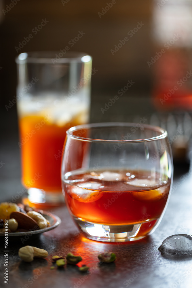 2 glasses of whisky with ice on dark background. Accessorised with dish of nuts and decorative drinks tray in background 2 glasses of whisky with ice on dark background. Accessorised with dish of nuts and decorative drinks tray in background