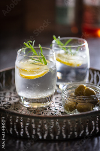 2 glasses of gin & tonic with bowl of olives on a drinks tray.  Drinks garnished with rosemary lemon and ice.