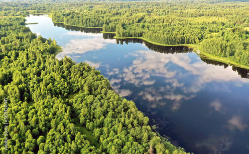 Aerial view of an elongated lake with winding coast and reflection of blue sky and clouds in water in the woods of Valday, Russia