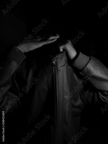 Man without face wearing leather jacket on a dark background. His hand is placed where his head should be. A real photograph, without manipulation.
