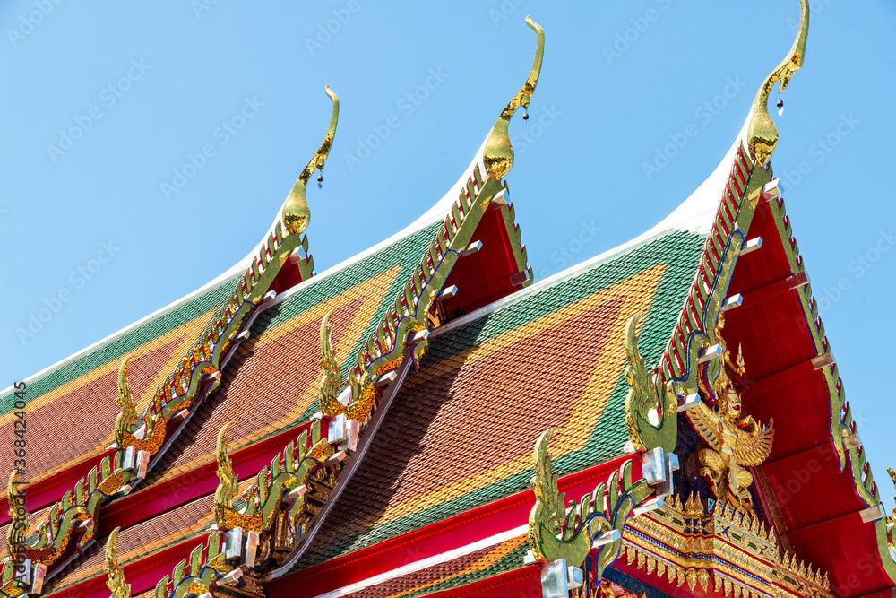 Fototapeta premium In Thailand most Buddhist temples are made using a lot of gold leaf-covered ornaments. The building itself is usually white with a tri-coloured roof in red, green and orange/dark yellow.