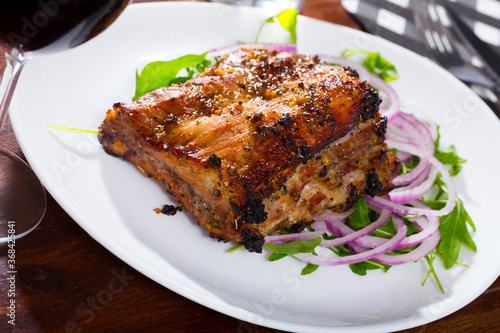 Baked under sauce tasty pork ribs at plate with arugula and onion salad