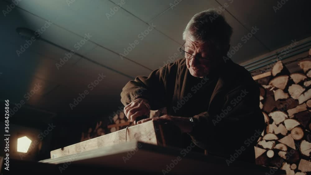 Old man removing a staple from a piece of wood in his cellar Old man removing a staple from a piece of wood in his cellar