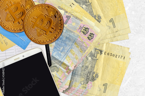 1 Ukrainian hryvnia bills and golden bitcoins with smartphone and credit cards. Cryptocurrency investment concept. Crypto mining or trading photo