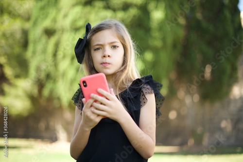 Portrait of a confused Caucasian  little girl  holding mobile phone and shrugging shoulders and frowning face.