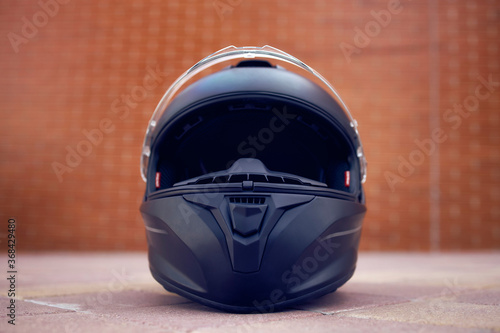 Close-up of a black helmet on the ground with the visor open. Front view.