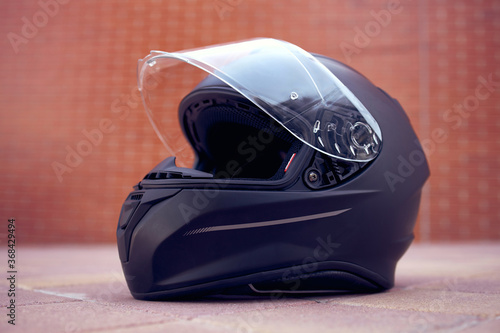 Close-up of a black helmet on the ground with the visor open. Side view.