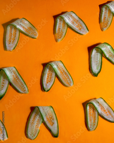 Long cucumber slices arranged on orange background. Pattern of thin cucumber slices on orange surface.