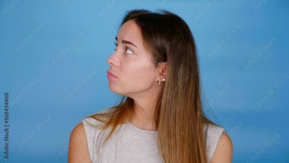 Beautiful woman in gray t-shirt looks around on blue background with copy space. 4K slow motion footage Beautiful woman in gray t-shirt looks around on blue background with copy space. 4K slow motion footage