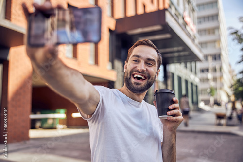 Fun man with coffee taking selfie outdoor