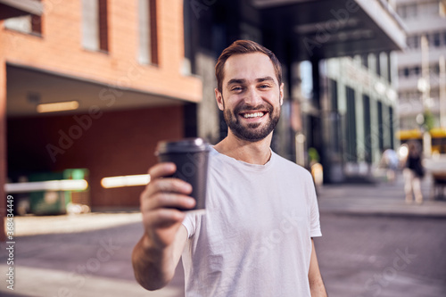 Waist up shot portrait of smiling guy with coffee outdoors