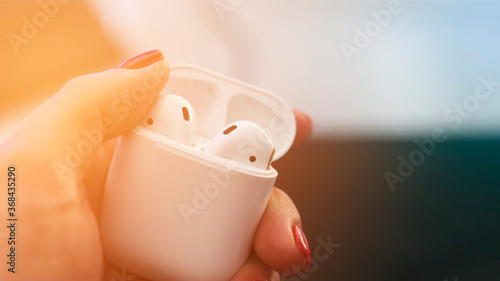 White case with wireless headphones in female hands. Close-up, sunlight. photo