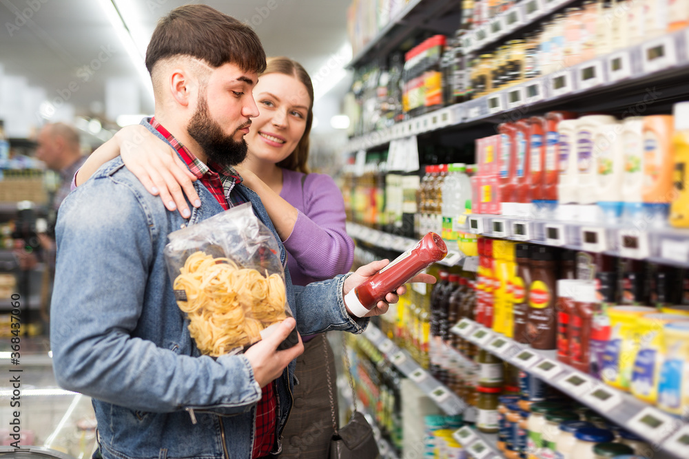 Portrait of young loving couple choosing products for family dinner in grocery store