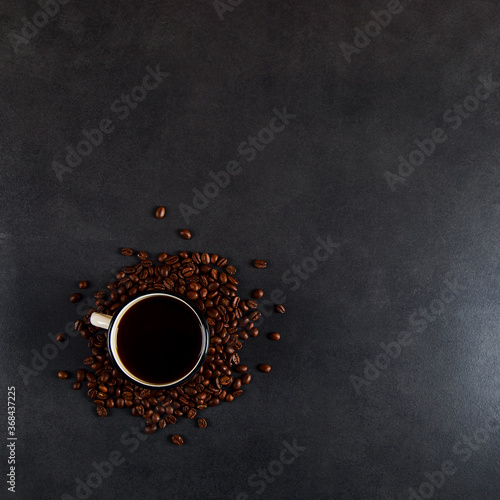 Black delicious coffee in an iron mug and scattered grains on a stone table. Authentic drink, copy space.