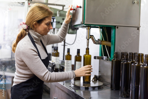 Billede på lærred Woman working on bottling conveyor of food producing factory, filling glass bott