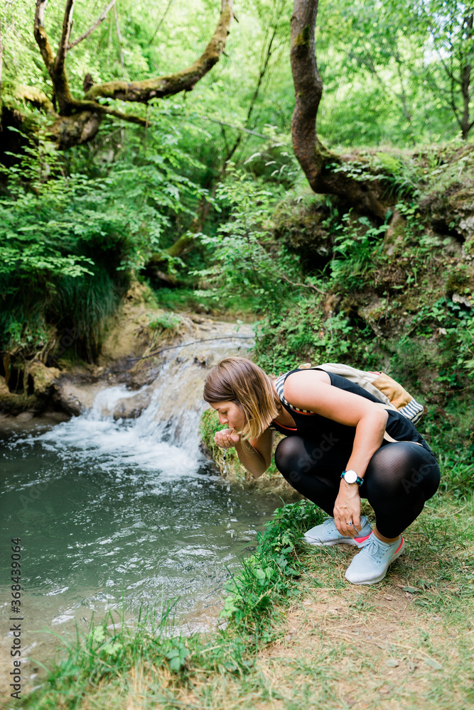 Fototapeta premium Young female nature explorer drinking water from the spring