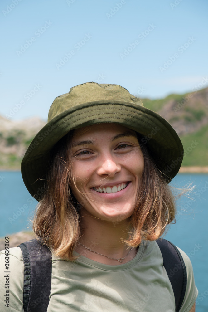 Portrait of young caucasian woman wearing a hat while trekking in the nature.