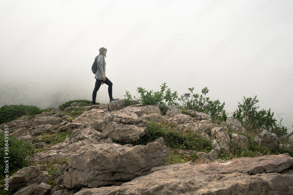 Young caucasian woman trekking over some rocks among the mist in the nature. Young caucasian woman trekking over some rocks among the mist in the nature.
