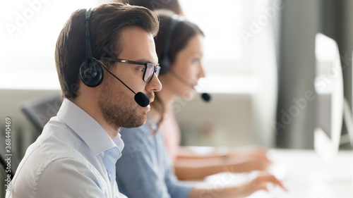 Confident call center operator agent in headset with microphone consulting client online close up, busy employee working in customer support service office, coworking space, horizontal photo