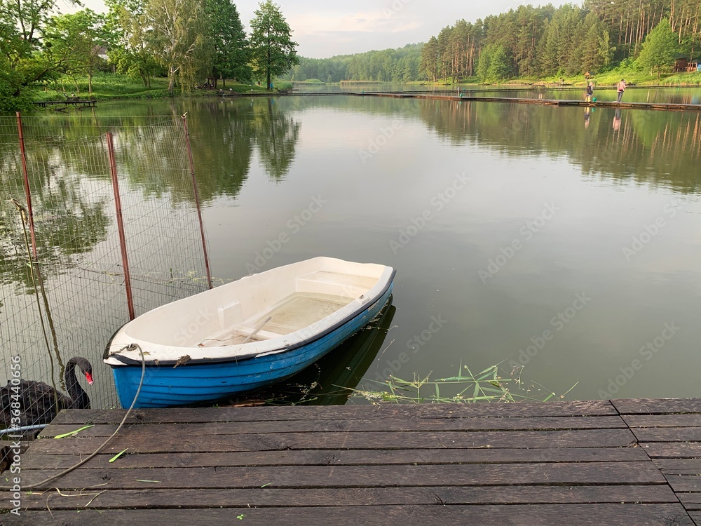 Wooden boat on the pier on the background of the lake. Fishing boat on the shore of a forest reservoir. The boat is tied to the shore. Concept: outdoor recreation, tranquility by the water.